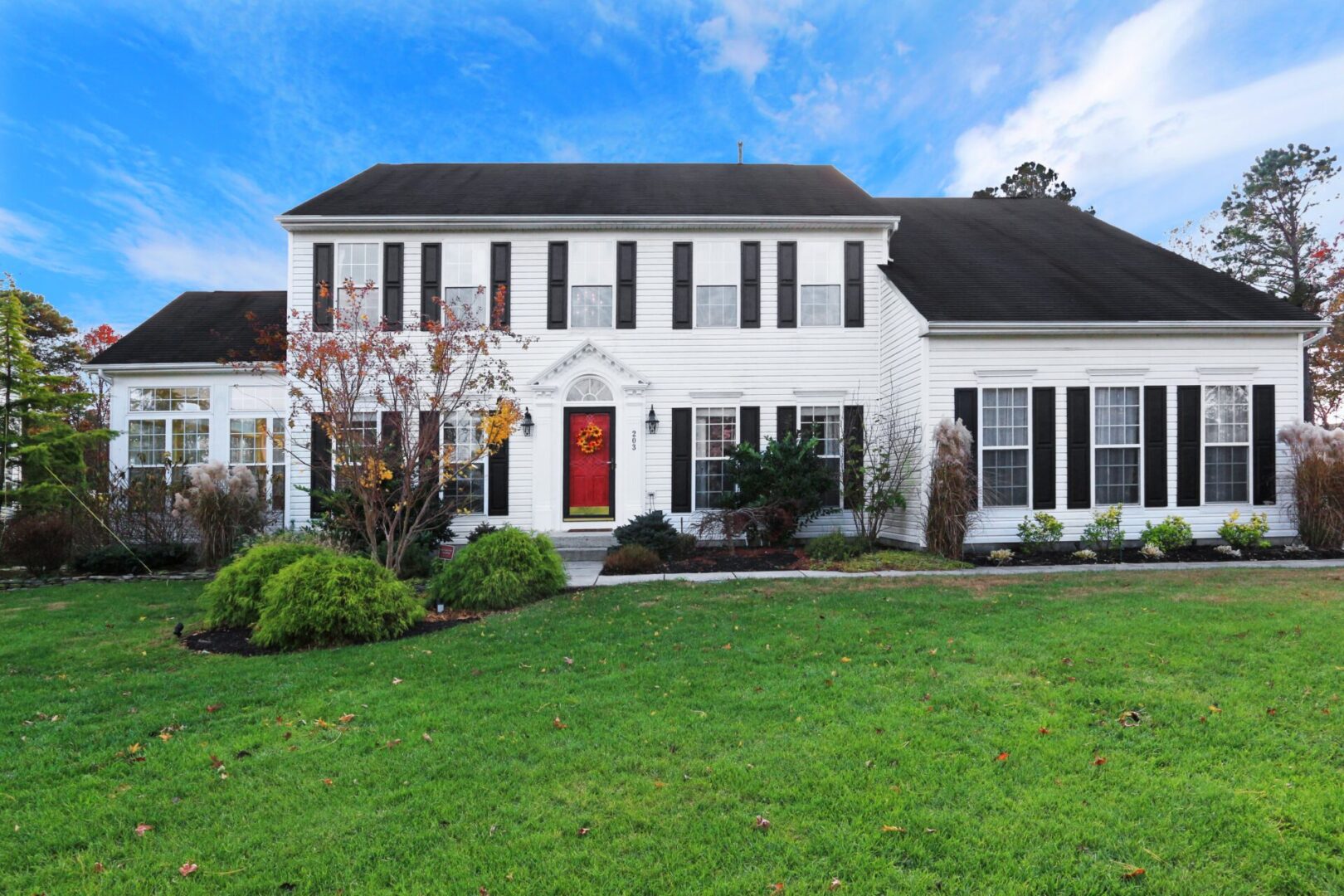 White colonial house with red door and lawn